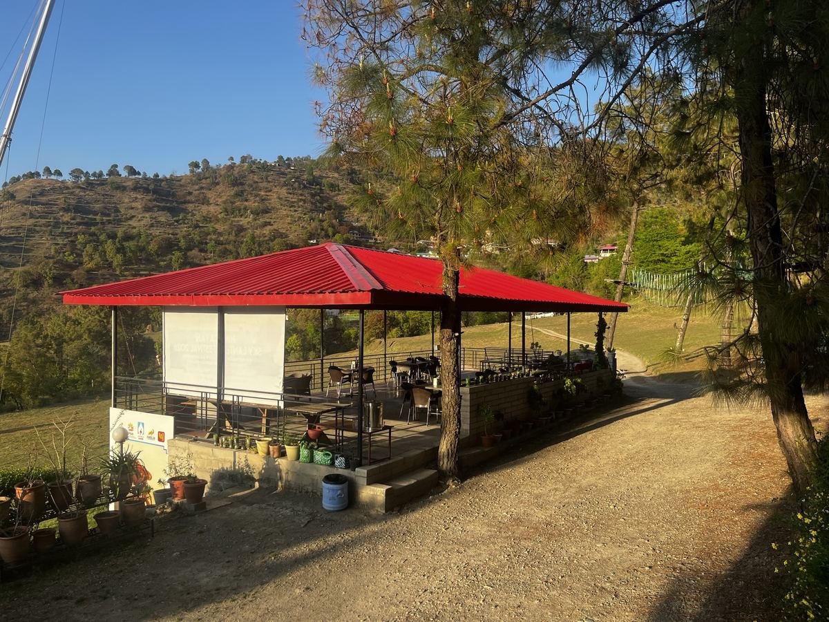 Open-air dining pavilion with a red roof among the pines at The Glide Inn, Junga, with terraced hills behind