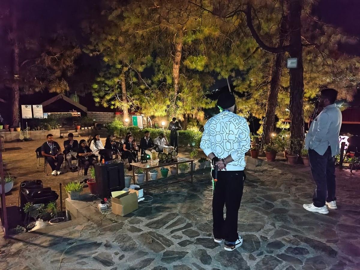 Hosts addressing a seated team on the stone terrace at night, with trophies on a table