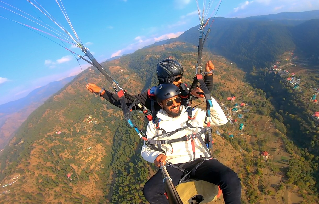 Male guest tandem paragliding with arms raised flying over valley near Shimla