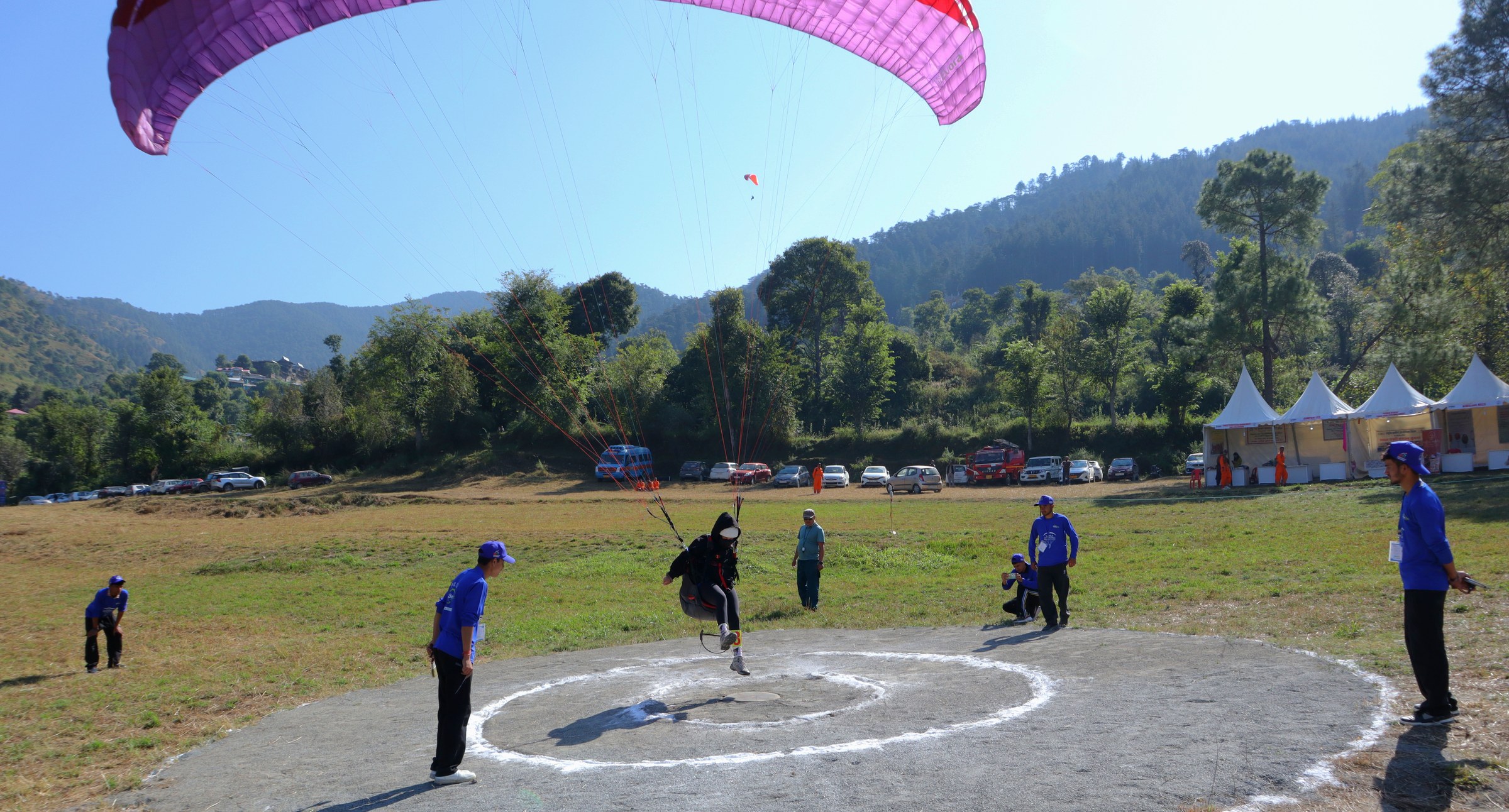 Pink paraglider landing on the circle with instructors at The Glide Inn Shimla