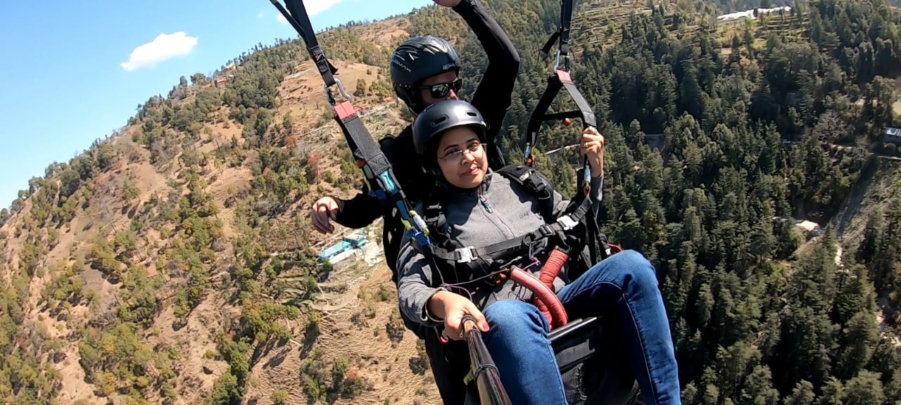 Female guest tandem paragliding with instructor over Himalayan pine valley near Shimla