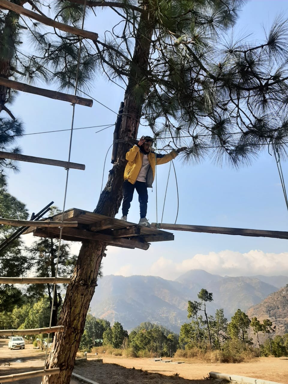 Guest in yellow jacket balancing on a tree top wooden beam with mountains in background