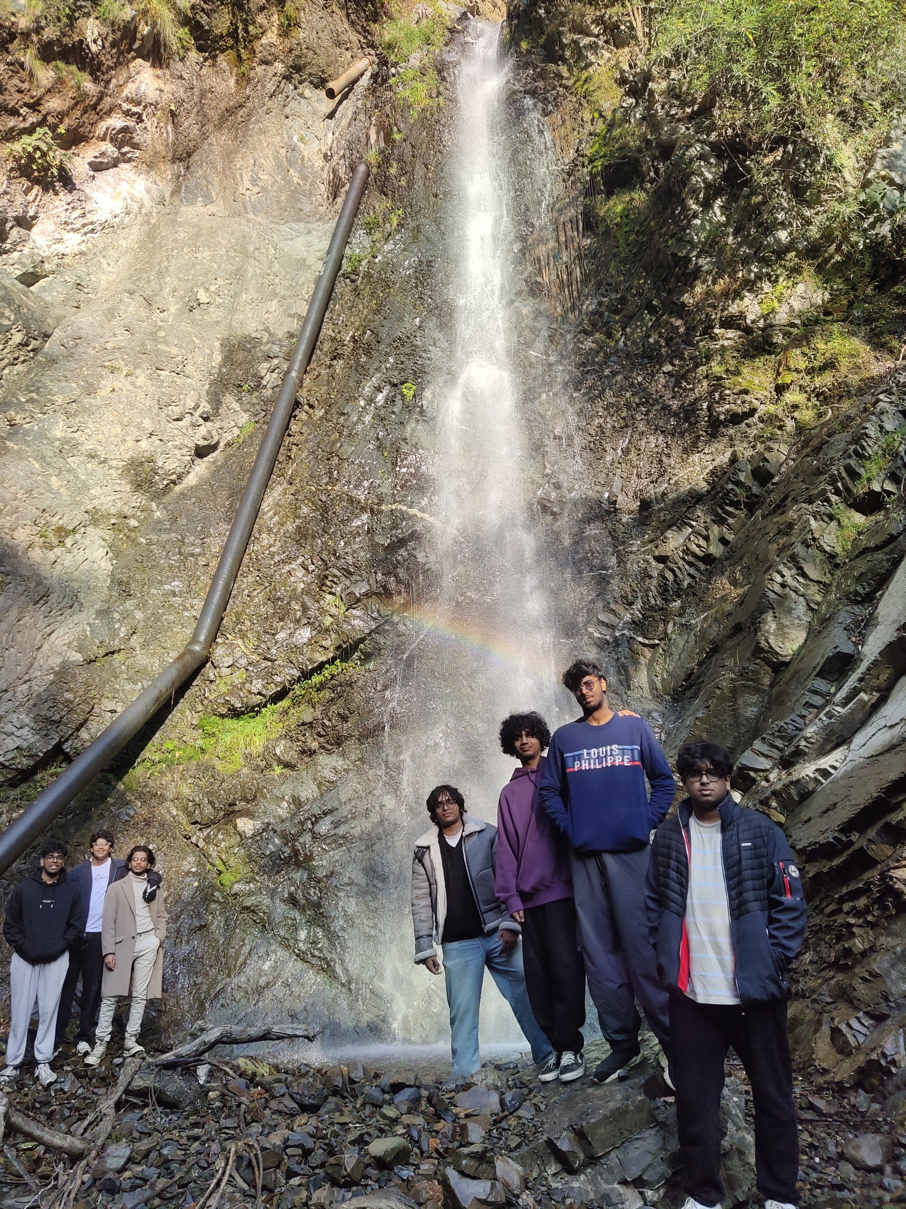 Group of guests posing at a waterfall with a rainbow on a trek near The Glide Inn Shimla